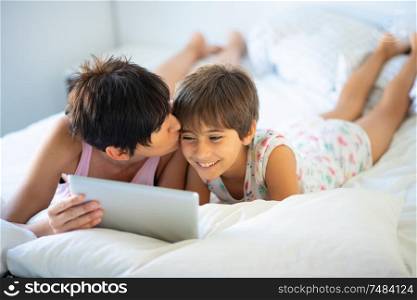 Middle-age mother with her eight years daughter using digital tablet in bedroom. Funny mom and lovely little girl are having fun on the bed.. Middle-age mother with her eight years daughter using digital tablet in bedroom.