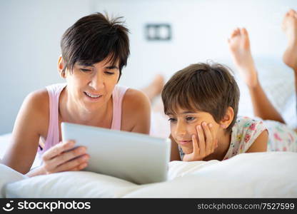 Middle-age mother with her eight years daughter using digital tablet in bedroom. Funny mom and lovely little girl are having fun on the bed.. Middle-age mother with her eight years daughter using digital tablet in bedroom.