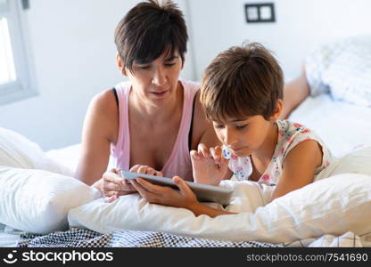 Middle-age mother with her eight years daughter using digital tablet in bedroom. Funny mom and lovely little girl are having fun on the bed.. Middle-age mother with her eight years daughter using digital tablet in bedroom.