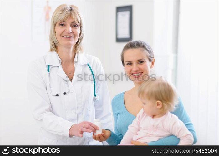 Middle age pediatric doctor giving tablets bottle to mother with baby