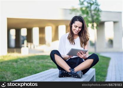 Middle-age woman using digital tablet sitting outdoors in urban background.. Young woman using digital tablet sitting outdoors in urban background.