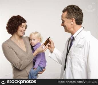 Middle-aged adult Caucasian male doctor handing Caucasian mother medication in a bottle.