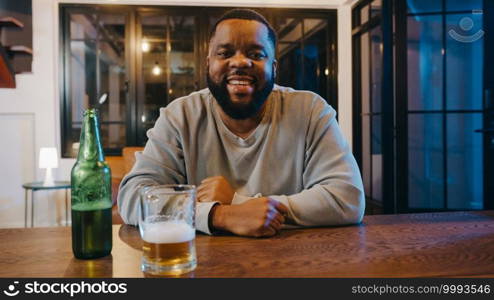 Middle-aged African American male drinking beer having fun happy moment night party event online celebration via video call at home. Social distancing, quarantine for coronavirus. Point of view or POV