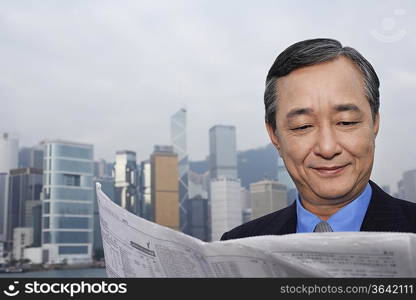 Middle-aged business man reading newspaper, office buildings in background