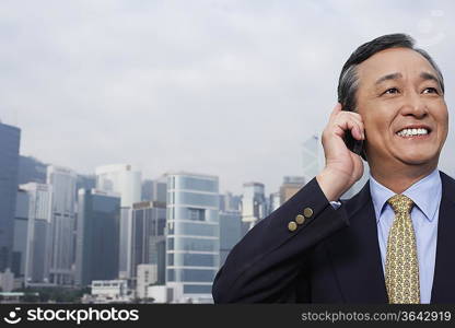 Middle-aged business man talking on mobile, office buildings in background