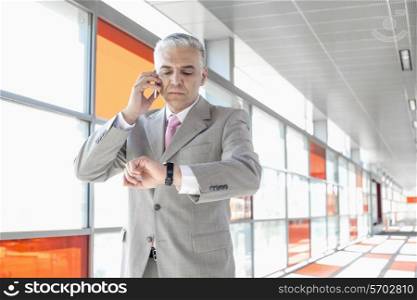 Middle aged businessman checking time while on call at railroad station