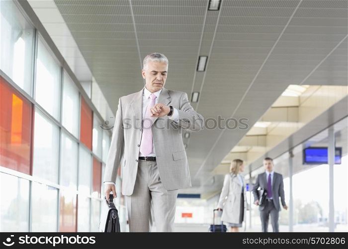 Middle aged businessman checking time with colleagues in background at railroad station