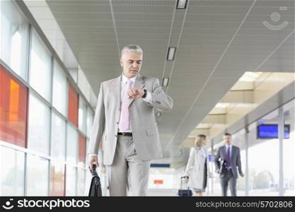 Middle aged businessman checking time with colleagues in background at railroad station