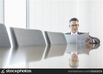 Middle-aged businessman reading book at conference table