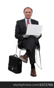 Middle-aged businessman sat in chair using laptop