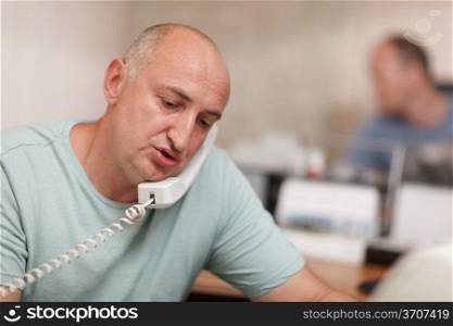 Middle-aged businessman speaking on the phone and working in the office