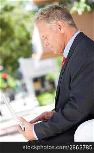 Middle-aged businessman using laptop outdoor