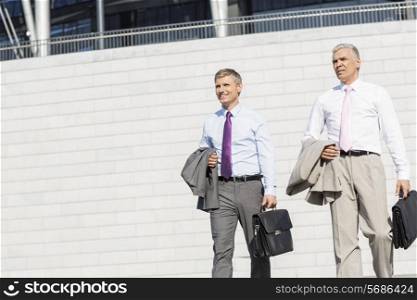 Middle-aged businessmen with briefcases against wall