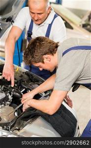 Middle aged car repairman helping colleague in garage
