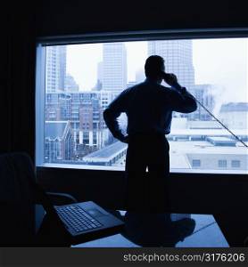 Middle-aged Caucasian male on phone in office with skyline in background.