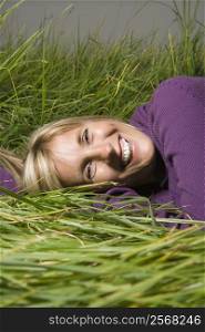 Middle-aged Caucasian woman lying in grass laughing.