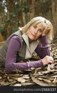 Middle-aged Caucasian woman lying on ground in forest.