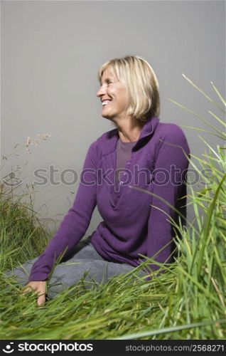 Middle-aged Caucasian woman sitting in field looking to side and smiling.