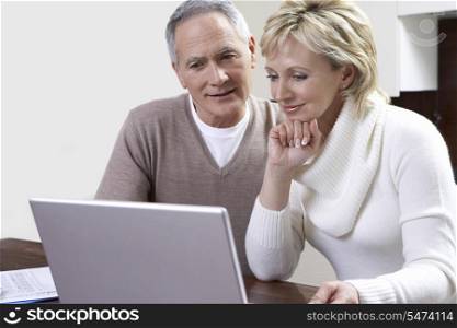 Middle-aged couple counting bills using laptop in kitchen