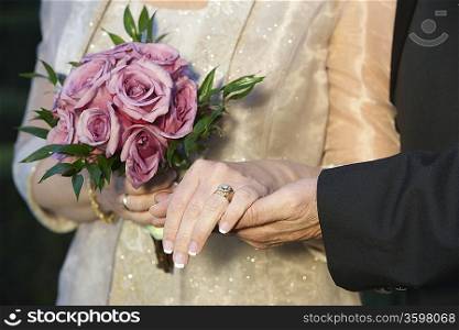 Middle-aged couple holding hands, woman holding bouquet, mid-section, close-up of hands