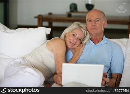 Middle-aged couple in bed with laptop