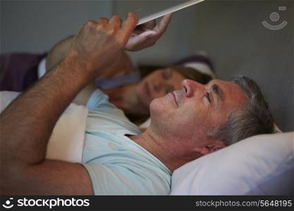 Middle Aged Couple In Bed With Man Using Tablet Computer