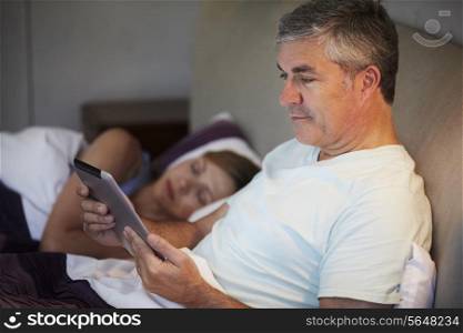 Middle Aged Couple In Bed With Man Using Tablet Computer