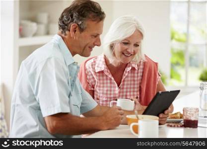 Middle Aged Couple Looking At Digital Tablet Over Breakfast