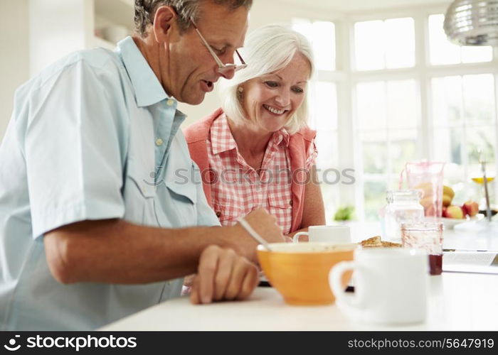 Middle Aged Couple Looking At Digital Tablet Over Breakfast