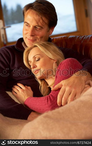 Middle Aged Couple Relaxing On Sofa In Chalet With Winter View