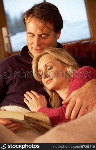 Middle Aged Couple Relaxing On Sofa In Chalet With Winter View
