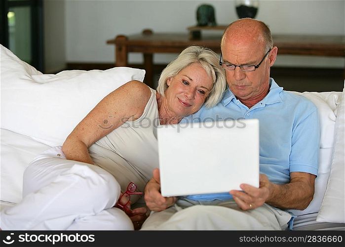 Middle-aged couple sat on sofa with laptop