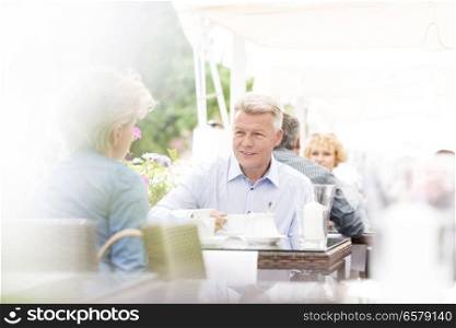 Middle-aged couple sitting at sidewalk cafe on sunny day