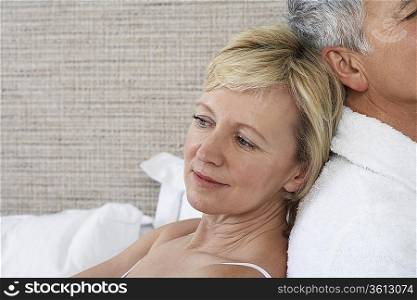 Middle-aged couple sitting back to back in bedroom, close-up