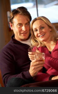 Middle Aged Couple Sitting On Sofa With Glasses Of Whisky