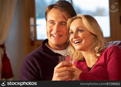 Middle Aged Couple Sitting On Sofa With Glasses Of Whisky Watching TV