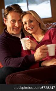 Middle Aged Couple Sitting On Sofa With Hot Drinks
