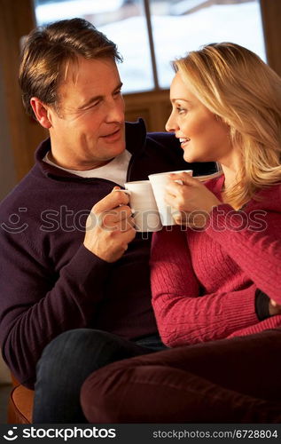 Middle Aged Couple Sitting On Sofa With Hot Drinks