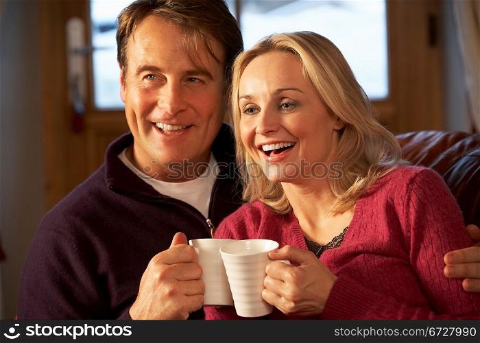 Middle Aged Couple Sitting On Sofa With Hot Drinks Watching TV