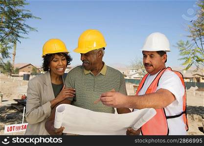 Middle-aged couple watching blueprints with surveyor
