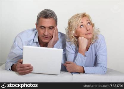 Middle aged couple with a laptop on their bed.