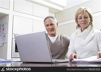 Middle-aged couple working on laptop in kitchen
