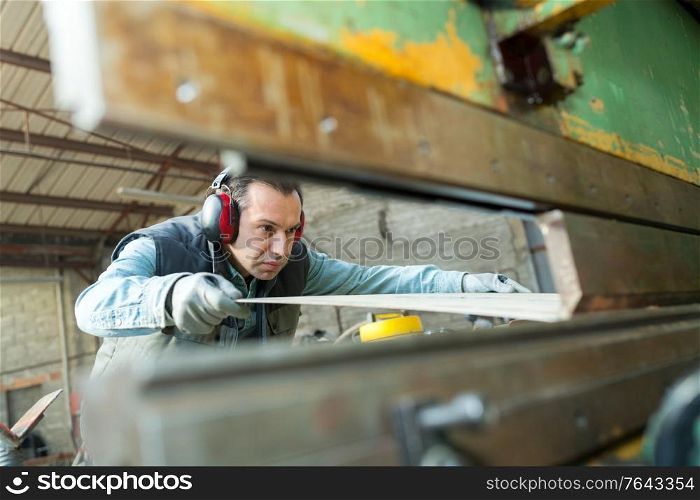 middle-aged male operative working with sheet metal viewed through machine