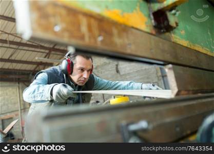 middle-aged male operative working with sheet metal viewed through machine