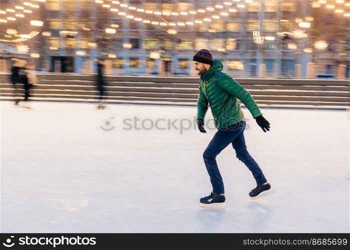 Middle aged male wears figure skates, being at ice rink in winter park, has fun with friend. Athlete speed skater demonstrates his talents on skating ring. Winter sport. Christmas vacations.