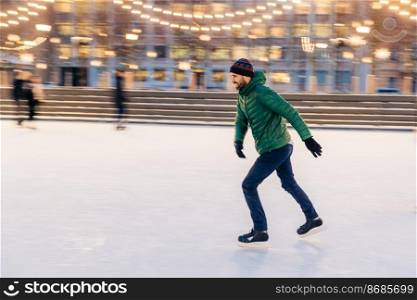 Middle aged male wears figure skates, being at ice rink in winter park, has fun with friend. Athlete speed skater demonstrates his talents on skating ring. Winter sport. Christmas vacations.