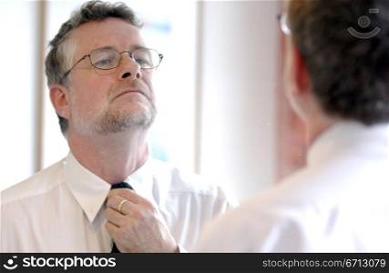 middle aged man adjusting tie in mirror