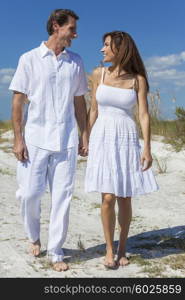 Middle aged man and woman romantic couple in white clothes walking on a deserted tropical beach with bright clear blue sky