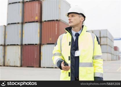 Middle-aged man holding walkie-talkie in shipping yard