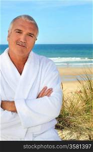 Middle aged man in a toweling robe by the sea